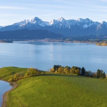 Green hills and trees on the shores of a quiet lake against the backdrop of majestic alpine