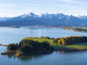 Idyllic mountain landscape with a calm lake, green hills and golden autumn trees under a blue sky