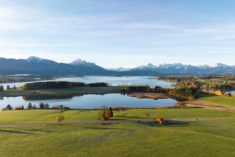 Extensive scene with lake and mountains, surrounded by green meadows and autumn colors,