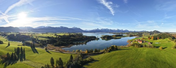 Wide panoramic view of a green landscape with lake and mountain backdrop under clear sky,