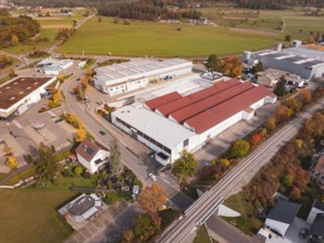 An industrial complex with red roofs and a railroad line, surrounded by autumn trees, Althengstett,