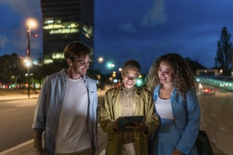 Diverse group of young adults walking a city sidewalk at night, smiling and sharing content on a