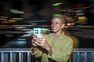 Smiling woman taking a video or picture with a smartphone, capturing the blurred light trails of a