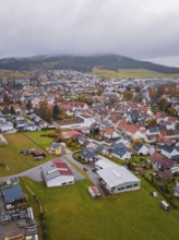 Small town with red roofs surrounded by fields and wooded hills under cloudy sky, Wehingen,