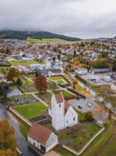 View of a town with church and cemetery surrounded by autumn trees and residential buildings on a
