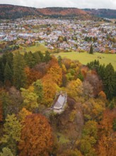 Small pavilion in a colorful autumn forest with a view of a city in the distance under cloudy sky,