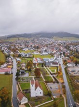 Town with white buildings and church, surrounded by trees, with wooded hills in the background