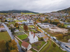 Urban view with church and residential buildings surrounded by autumn trees and mountains under a