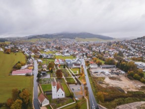 Aerial view of a village with church surrounded by fields, roads and wooded hills under a thick