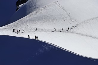 A group of mountaineers runs across a snow-covered mountain, Aiguille du Midi, Chamonix-Mont-Blanc,