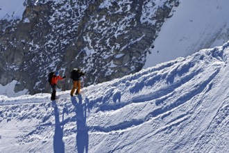 Two mountaineers run across a snow-covered mountain ridge, Aiguille du Midi, Chamonix-Mont-Blanc,