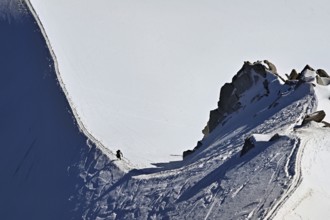 A mountaineer climbs over a snow-covered mountain ridge, Aiguille du Midi, Chamonix-Mont-Blanc,