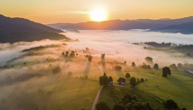 Sunrise over a fog covered village in a rural landscape, golden morning light, serene autumn