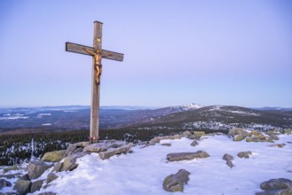 Christian cross on the peak of Mount Lusen with the view over the hills of the bavarian forest at