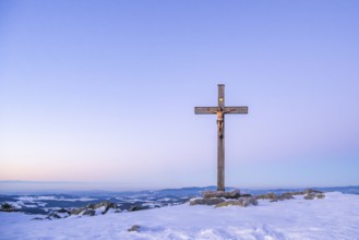Christian cross on the peak of Mount Lusen with the view over the hills of the bavarian forest at