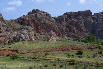 Church on green meadow against dramatic rocky backdrop under blue sky, Noravank monastery, Surb