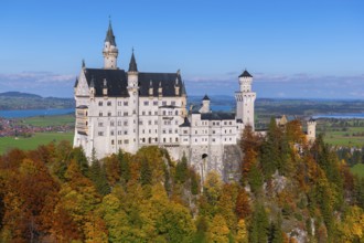 Impressive Neuschwanstein Castle in autumn landscape, surrounded by colorful trees and under blue