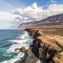 Desert landscape converges with ocean along a rugged coastal area, shore break at cliffs, blue