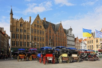 Historic houses on the market square in the old town of Bruges with horse-drawn carriages, Grote