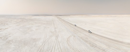 Aerial view, two off-road cars driving on a salt pan, arid landscape, Botswana