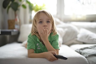 Child, boy, 7 years old, blonde, lying on sofa with remote control in hand, watching TV, watching