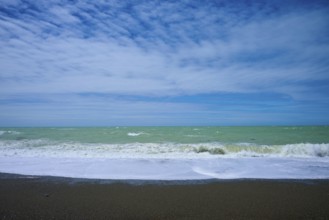 Wavy beach with calm sky in the background, Tuhawaiki Point Lighthouse or Jack's Point Lighthouse,