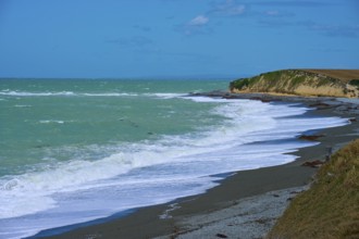 Waves crash against a rocky coast with blue sky, Tuhawaiki Point Lighthouse or Jack's Point