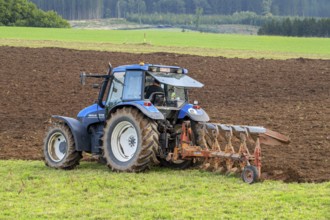 Tractor with plough, agricultural ploughing machine working on a field in autumn, fall in the