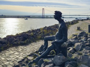 Photo with melancholy mood of bronze sculpture Poortekerl looking at Rhine waiting for ship to