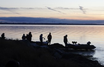 Angler on the beach during sunset, an angler docks on the shore with his inflatable boat and dog,