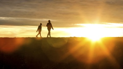 Woman and child walk across a dike on the island of Fehmarn at sunset, 13.10.2025, Fehmarn,