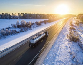 Petrol cargo truck lorry tanker driving on highway hauling oil products at sunrise, wide snowy