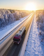 Petrol cargo truck lorry tanker driving on highway hauling oil products at sunrise, wide snowy