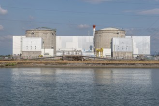 A large industrial nuclear power plant is located on a quiet water front. Two tall cylindrical