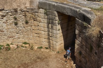 Visitor walks through huge stone gate, Mycenaean domed tomb, archaeological site, UNESCO World
