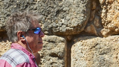 Visitor wearing sunglasses stands in front of the huge stone walls of the Lion Gate, Archaeological