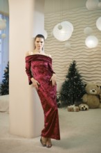 A woman wearing a luxurious red off-shoulder gown stands confidently in a tastefully decorated