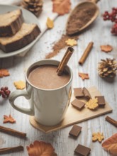 A cup of hot chocolate with cinnamon sticks, cake and autumn decorations
