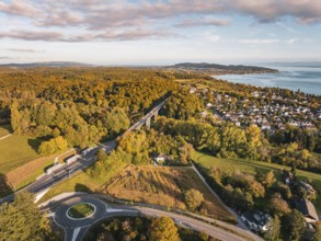 Highway through a forest, with a view of a nearby town and the lake on the horizon under clouds,