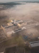 Aerial view of a complex of buildings in thick morning fog, modernly embedded in a natural