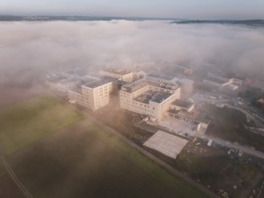 Large industrial buildings surrounded by fields under a thick layer of fog, new hospital health