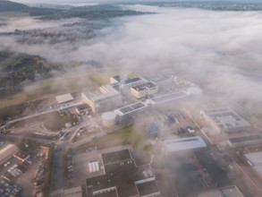 Wide angle view of an industrial center in fog surrounded by natural landscape at dawn, new