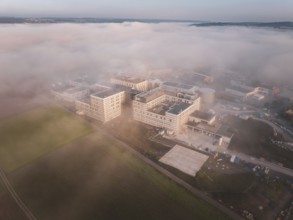 Industrial buildings seen from the air in morning fog, surrounded by natural landscape at dusk, new
