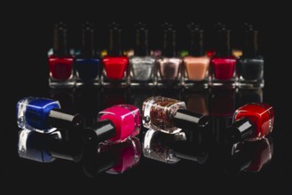 Different nail polish bottles in intense colors on a black surface with reflection