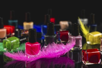 Colourful nail polish bottles and coloured feathers on black surface with reflection