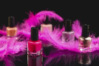 Pink and pink nail polishes with pink feathers on black surface with reflection