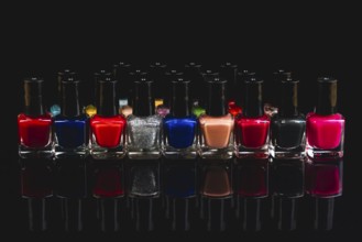A variety of nail polish bottles in different colors with reflections on a black background