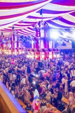 Marquee full of people in traditional Bavarian traditional costume with colourful lighting and