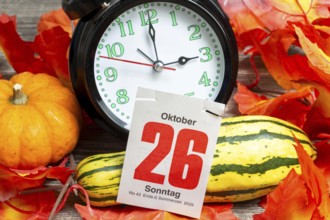 Time changeover to winter time 2025: Close-up of an alarm clock, autumnal decoration and a page