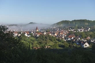 Idyllic village with church surrounded by hills, morning mist and green landscape, Rems Valley,